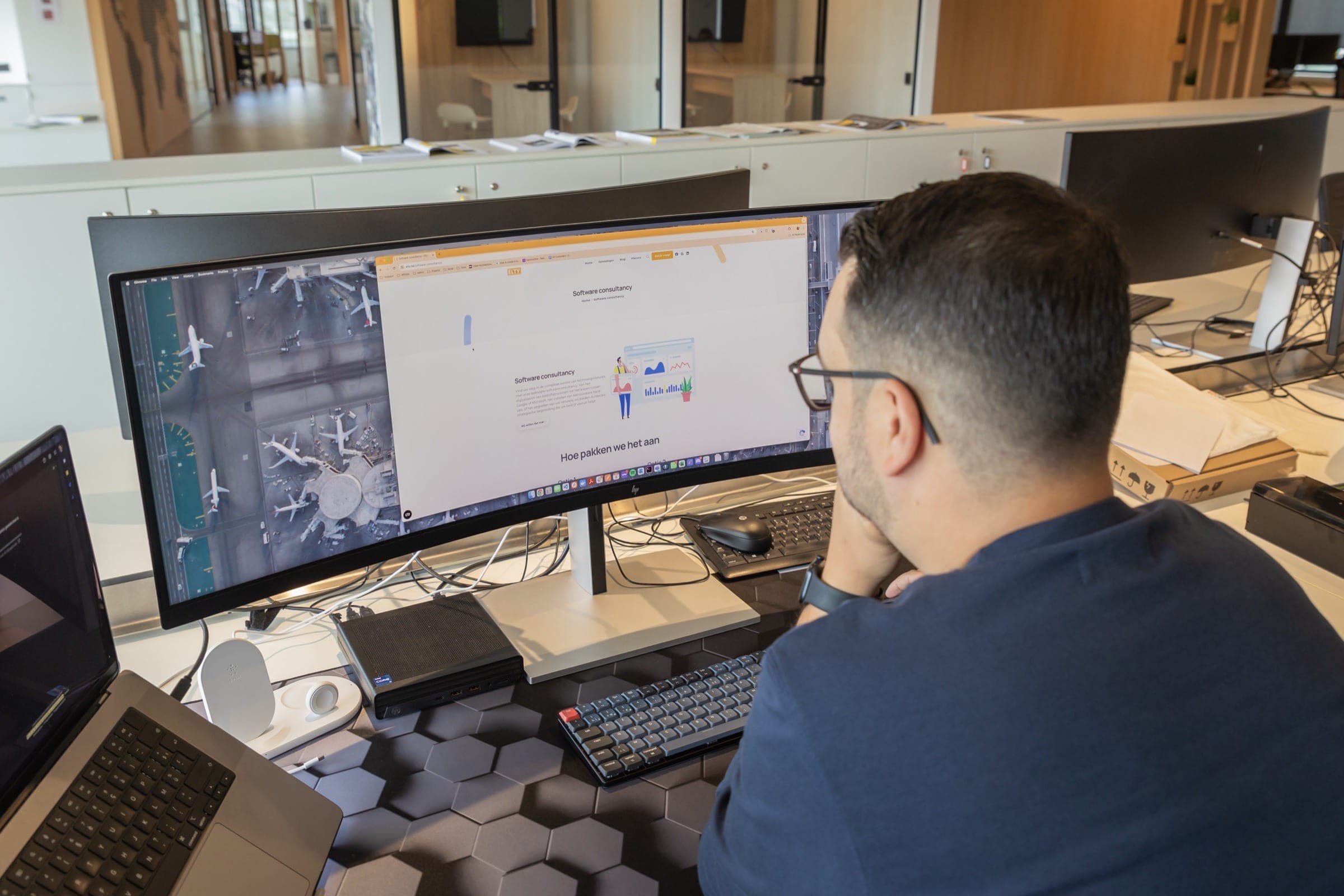 Tyas aan het werk aan zijn bureau met grote monitors