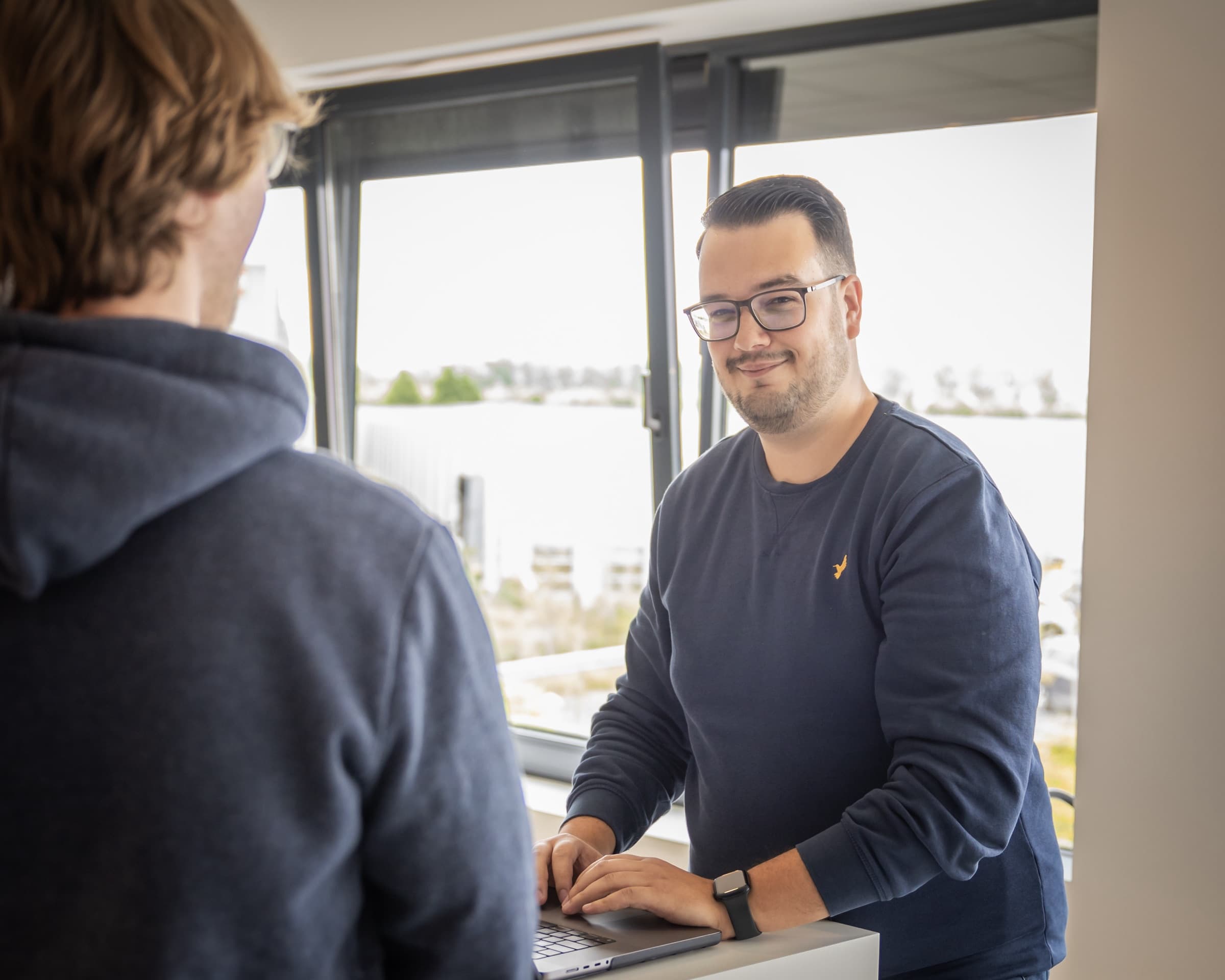 Tyas voert een gesprek met een klant aan een hoge tafel met uitzicht
