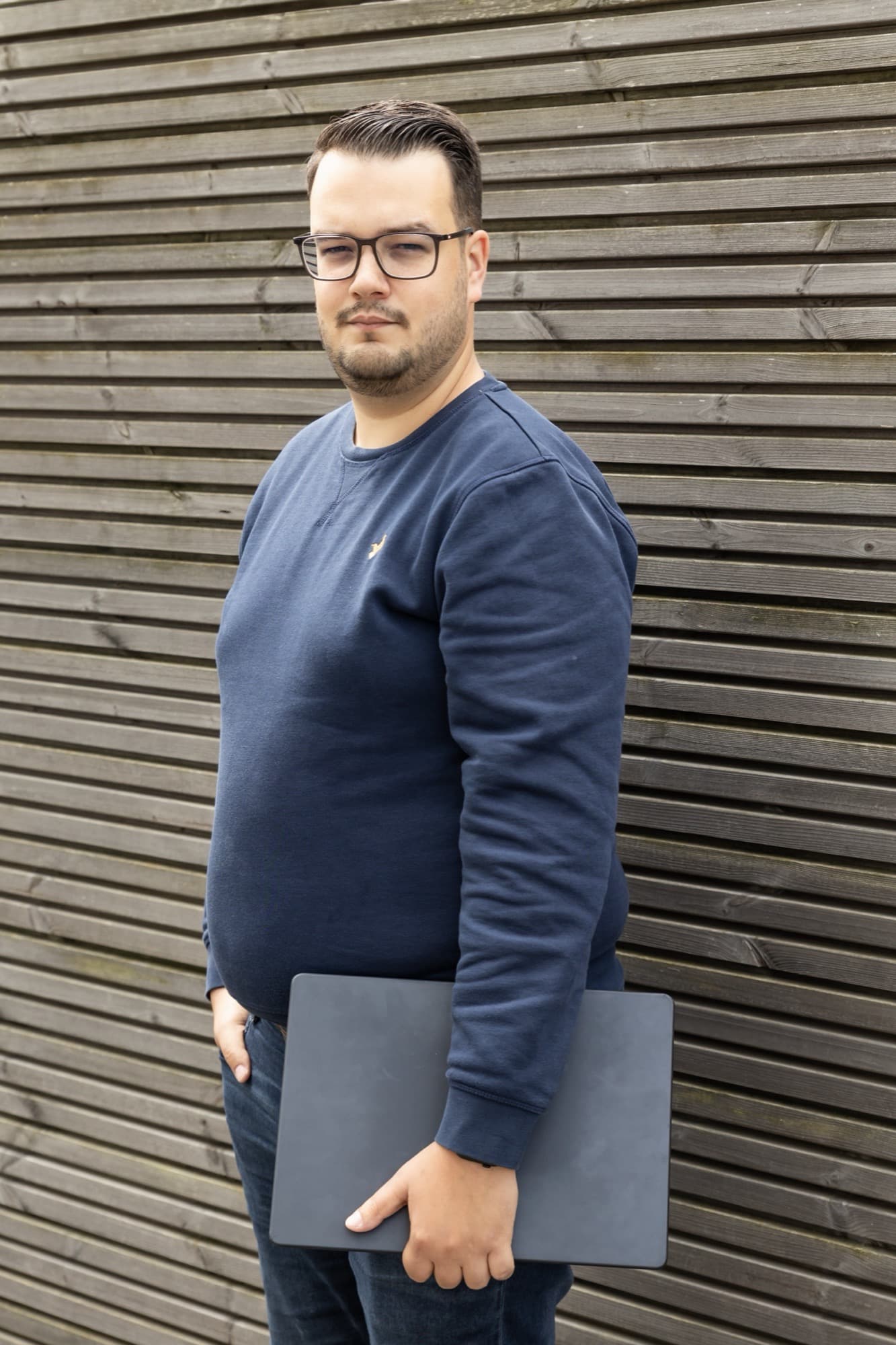Tyas staat buiten met zijn laptop, gekleed in bedrijfskleding